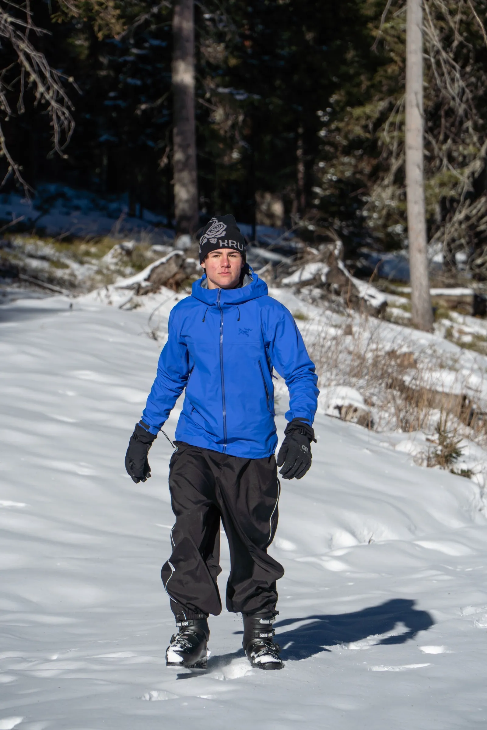 Person in blauer Jacke und schwarzer Hose auf einer Schneefläche im Wald